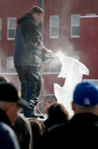 a man carving an ice Sculpture and others looking at it